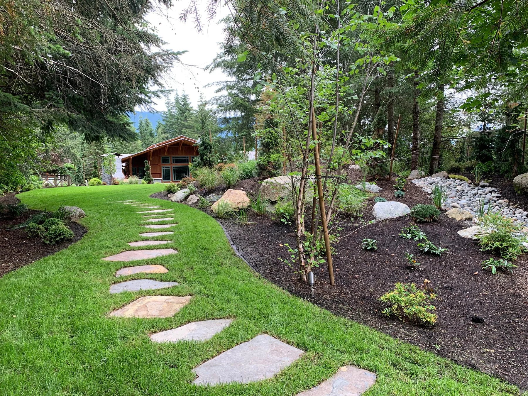 Stepping stones curve through a green lawn toward a timber home.