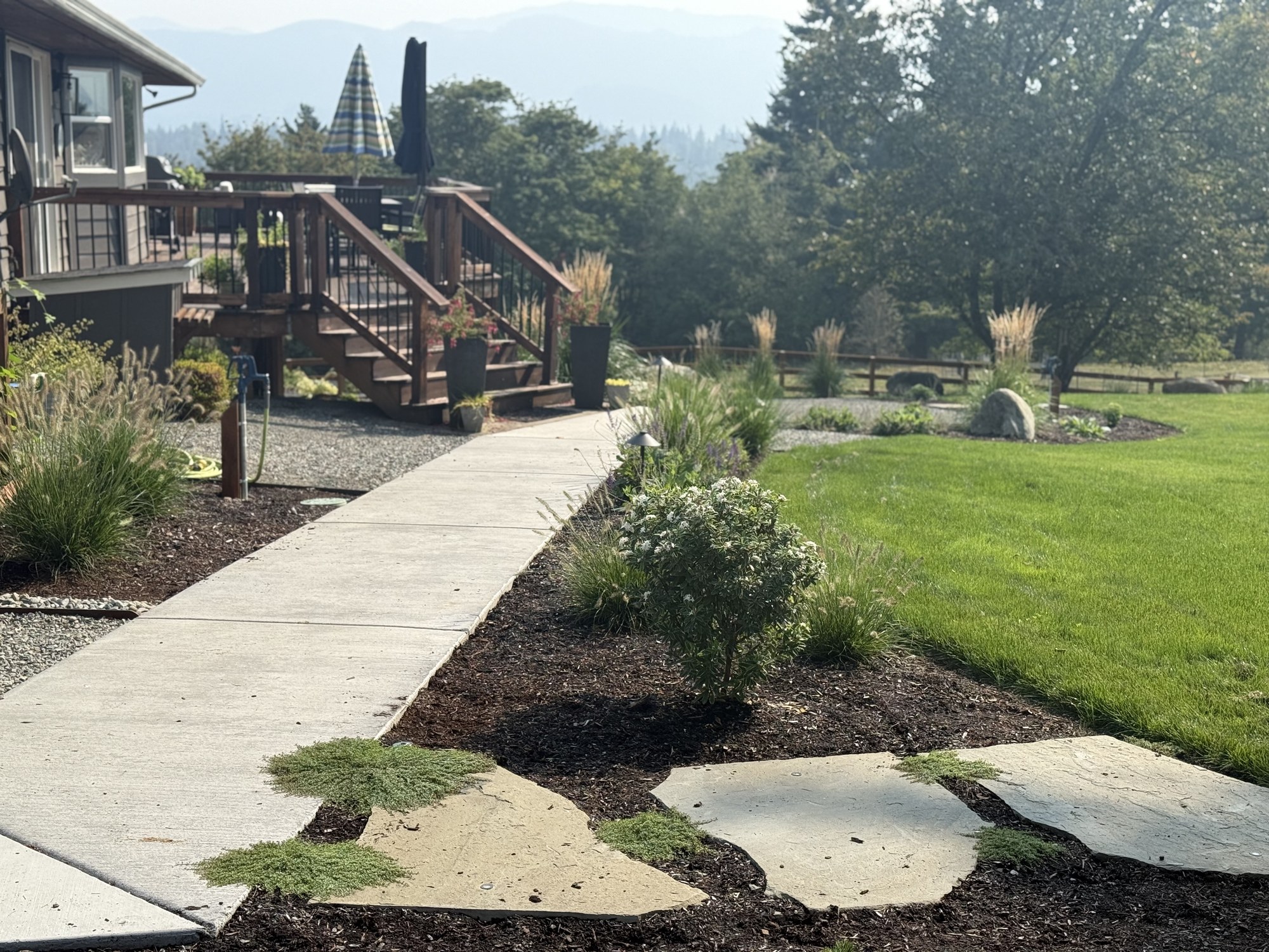 A concrete walk connects the deck to lawn and planting, with natural stone stepping stones in the foreground.